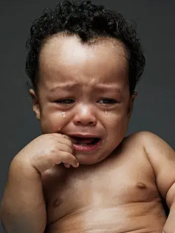 Bé trai da đen chống cằm ngồi khóc
